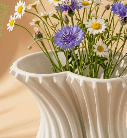 Close-up of a white sculptural vase with ribbed swirl pattern holding colorful wildflowers, ideal for floral decor.