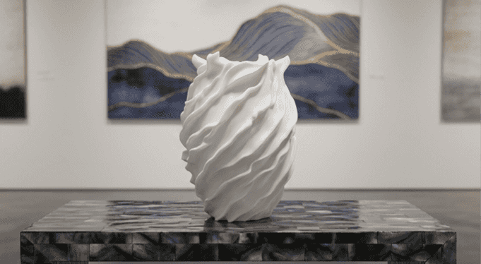 The Flow Vessel in white - sculptural twisted wave vase displayed in gallery setting on marble plinth